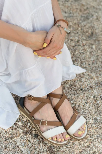 stock image Girl sits on beach and holding knees. Sandals in Greek style. Vertical frame.