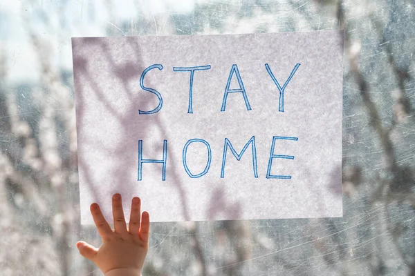 Inscription STAY HOME in children\'s hand on the window glass. Quarantine isolation.