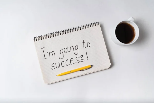 Im going to success inscription. Notebook, pen and cup of coffee. White background