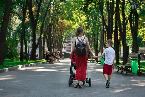 Mom walks in the Park with stroller and elder son. Walk with children. Childhood Lifestyle.