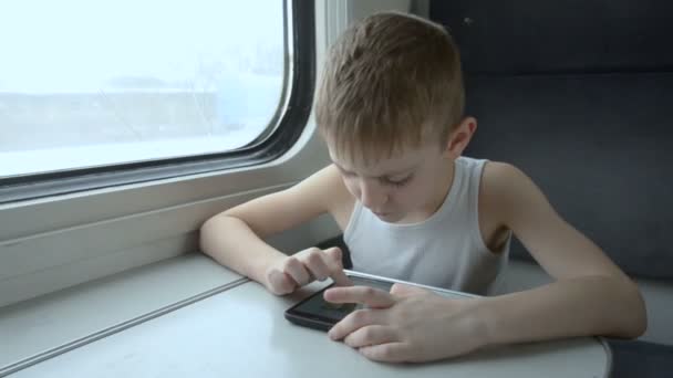 Niño viajando en el tren y utiliza el teléfono inteligente. Invierno fuera de la ventana — Vídeos de Stock