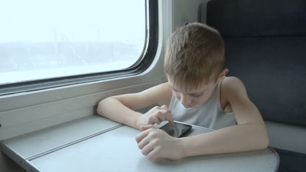 Μικρό αγόρι που ταξιδεύει με το τρένο και χρησιμοποιεί το smartphone. Χειμώνας έξω από το παράθυρο — Αρχείο Βίντεο