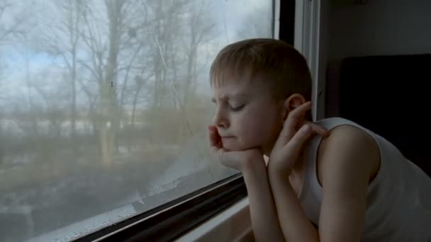 Figyelmes kisfiú, aki vonaton utazik, és kinézett az ablakon. Tél az ablakon kívül — Stock videók