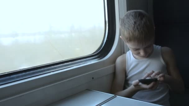 Μικρό αγόρι που ταξιδεύει με το τρένο και χρησιμοποιεί το smartphone. Χειμώνας έξω από το παράθυρο — Αρχείο Βίντεο