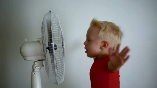 Mooie glimlachende blonde jongen in rood shirt geniet van koele lucht. Zomer concept. Langzame beweging — Stockvideo