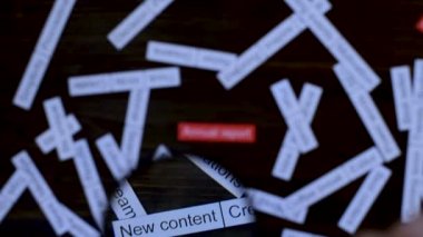 Büyüteçle el, yıllık rapora odaklanıyor. Çözüm bulmak. Koyu tahta masada etiket bulutu.