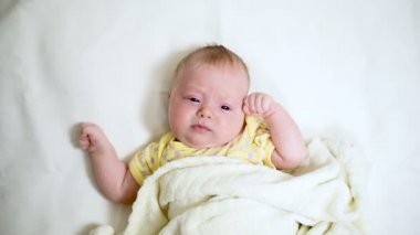 Yeni doğmuş şirin bebek yatakta uzanıp kameraya bakıyor. Anne saçlarını yumuşak tarakla tarıyor..