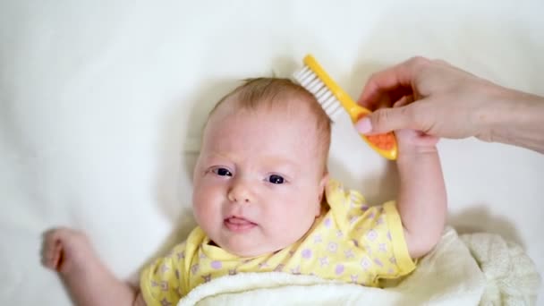 Main féminine caressant la tête du nouveau-né avec une brosse douce. Bébé paisible couché au lit et regardant la caméra . — Video