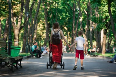 Genç anne, bebek ve büyük oğluyla Park 'ta yürüyor. Anne oğlunun elini tutuyor. Annelik kavramı.
