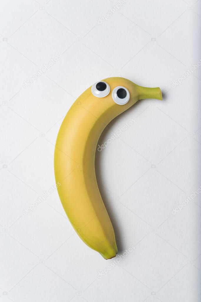 banana with funny face and Googly eyes on white background. Vertical frame.