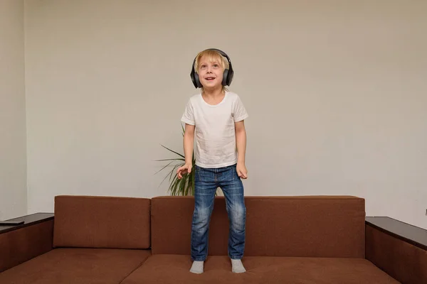 Αγόρι Στέκεται Στον Καναπέ Ακουστικά Παιδί Ακούει Μουσική Και Χορεύει — Φωτογραφία Αρχείου
