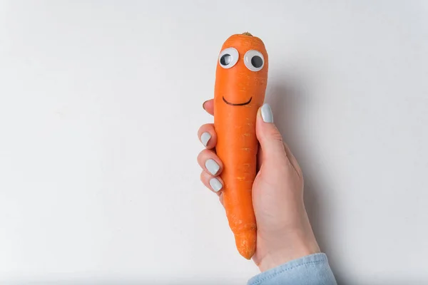 Carrot with funny face in hand on white background. Carrot character with Googly eyes