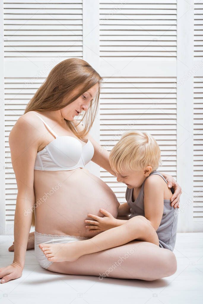 Beautiful young pregnant woman sitting on floor with her eldest son. Vertical frame.