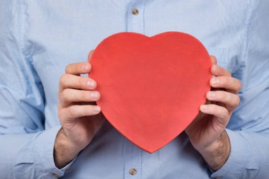 Erkek ellerinde kalp şeklinde büyük kırmızı bir kutu. Sevgili için bir hediye. Sevgililer Günü hediyesi..