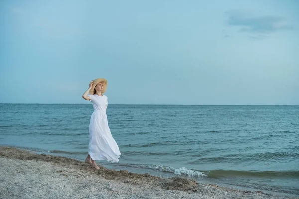Aristocrat woman in long white dress walks on beach. Nautical vacation.