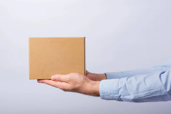 白い背景に腕の長さの箱を持っている男 正方形の段ボール箱 小包の配達 サイドビュー — ストック写真
