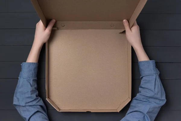 Empty open box of pizza in children\'s hands. Black background. Top view. Copy space