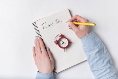 Kadının üst görünümü deftere yazma zamanını yazar. Not defteri ve klasik çalar saat. Planlama kavramı.