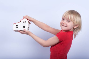 Gülümseyen çocuk model evi tutuyor. Ev almak, ipotek konsepti.