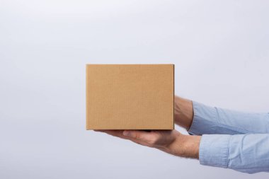 Kutuyu kol mesafesinde tutan adam. Beyaz arka plan. Kare karton kutu. Paketlerin teslimatı. Yan görünüm