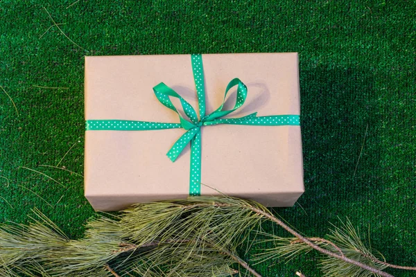 Δώρο τυλιγμένο σε χαρτί Kraft σε πράσινο φόντο με κλαδιά κέδρου. — Φωτογραφία Αρχείου