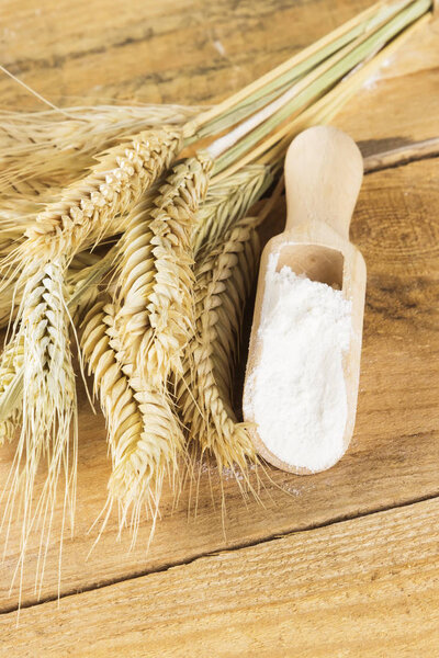 Мука и пшеничные уши на деревянном фоне
