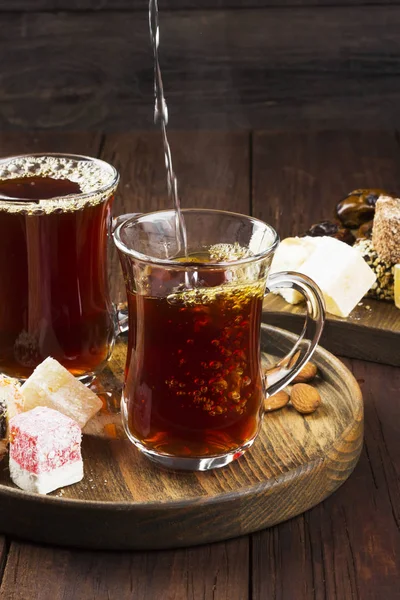 Chá preto, doces orientais, tâmaras e nozes em umas costas de madeira escuras — Fotografia de Stock