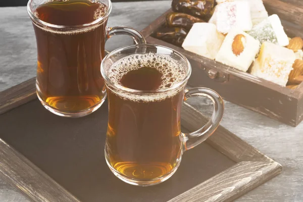 Zwarte thee, oosterse snoepjes, datums en noten op een donkere achtergrond. — Stockfoto
