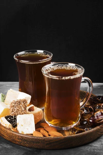 Zwarte thee, oosterse snoepjes, datums en noten op een donkere achtergrond. — Stockfoto