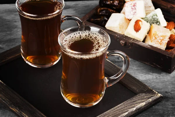 Черный чай, восточные сладости, финики и орехи на темном фоне . — стоковое фото