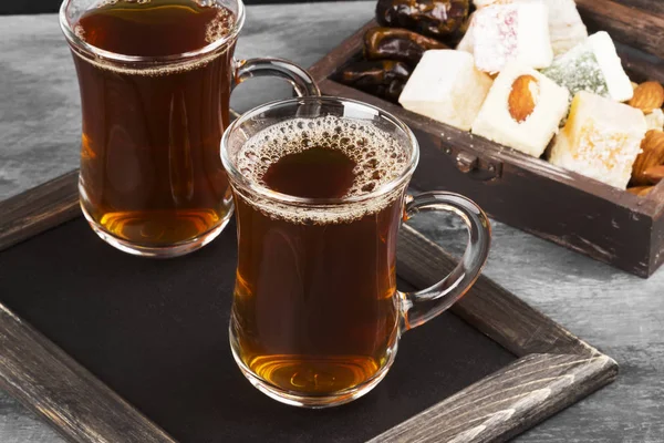 Zwarte thee, oosterse snoepjes, datums en noten op een donkere achtergrond — Stockfoto