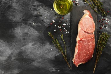 Sığır eti biber, zeytin yağı ve koyu arka plan üzerinde bir kekik ile kayrak bir gemide çiğ et parçası. Görünümü en çok, uzay kopyalayın. Gıda arka plan. Tonlama.