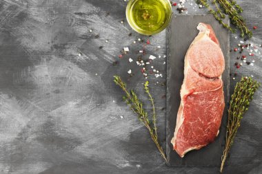 Sığır eti biber, zeytin yağı ve koyu arka plan üzerinde bir kekik ile kayrak bir gemide çiğ et parçası. Görünümü en çok, uzay kopyalayın. Gıda arka plan.