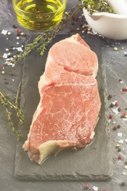 Sığır eti biber, zeytin yağı ve koyu arka plan üzerinde bir kekik ile kayrak bir gemide çiğ et parçası. Gıda arka plan. Tonlama