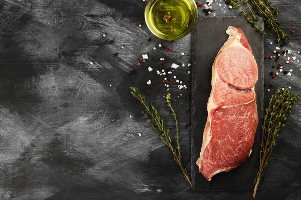 Sığır eti biber, zeytin yağı ve koyu arka plan üzerinde bir kekik ile kayrak bir gemide çiğ et parçası. Görünümü en çok, uzay kopyalayın. Gıda arka plan. Tonlama.