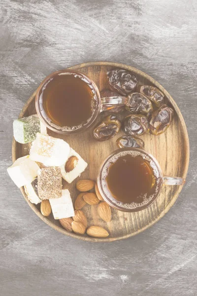 Chá preto, doces orientais, tâmaras e nozes num fundo escuro. Vista superior. Fundo alimentar. Tonificação . — Fotografia de Stock