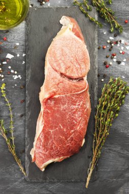 Sığır eti biber, zeytin yağı ve koyu arka plan üzerinde bir kekik ile kayrak bir gemide çiğ et parçası. Üstten Görünüm. Gıda arka plan