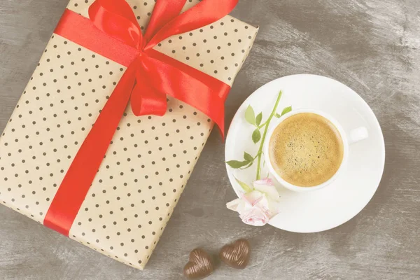 Espresso-Kaffee in einer weißen Tasse, eine rosa Rose, ein Geschenk mit rotem Band und Pralinen auf dunklem Hintergrund. Ansicht von oben. Lebensmittel-Hintergrund. Straffung — Stockfoto