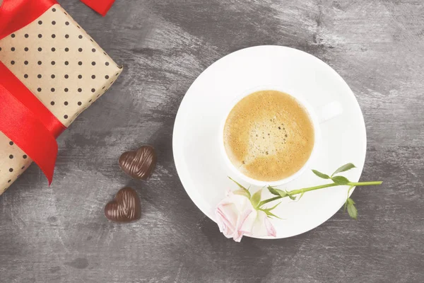 Espresso-Kaffee in einer weißen Tasse, eine rosa Rose, ein Geschenk mit rotem Band und Pralinen auf dunklem Hintergrund. Ansicht von oben. Lebensmittel-Hintergrund. Straffung. — Stockfoto