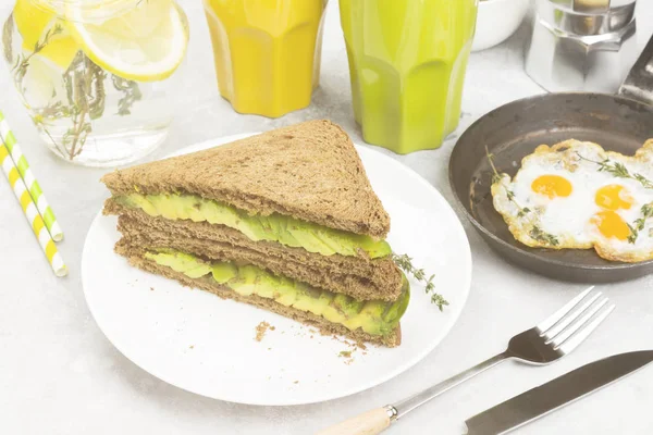 Café da manhã - um brinde de pão de centeio com abacate, ovos fritos, limonada e café em um contexto leve. Tonificação . — Fotografia de Stock