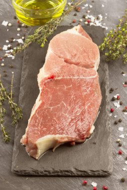 Sığır eti biber, zeytin yağı ve koyu arka plan üzerinde bir kekik ile kayrak bir gemide çiğ et parçası. Tonlama