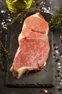 Sığır eti biber, zeytin yağı ve koyu arka plan üzerinde bir kekik ile kayrak bir gemide çiğ et parçası. Tonlama