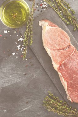 Sığır eti biber, zeytin yağı ve koyu arka plan üzerinde bir kekik ile kayrak bir gemide çiğ et parçası. Görünümü en çok, uzay kopyalayın. Gıda arka plan. Tonlama.