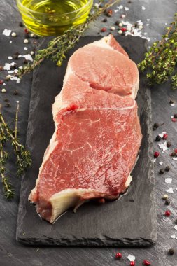 Sığır eti biber, zeytin yağı ve koyu arka plan üzerinde bir kekik ile kayrak bir gemide çiğ et parçası.