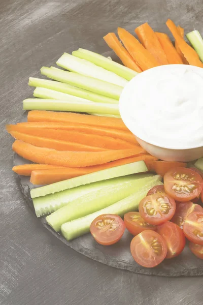 Кремовый соус в белой миске и различные овощи (помидоры, сельдерей, огурцы, морковь) на темном фоне. Тонирование — стоковое фото