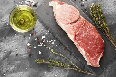 Sığır eti biber, zeytin yağı ve koyu arka plan üzerinde bir kekik ile kayrak bir gemide çiğ et parçası. Görünümü en çok, uzay kopyalayın. Gıda arka plan.