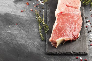 Sığır eti biber ile kayrak bir gemide ve karanlık bir arka plan üzerinde bir kekik çiğ et parçası. Uzay kopyalayın. Gıda arka plan.