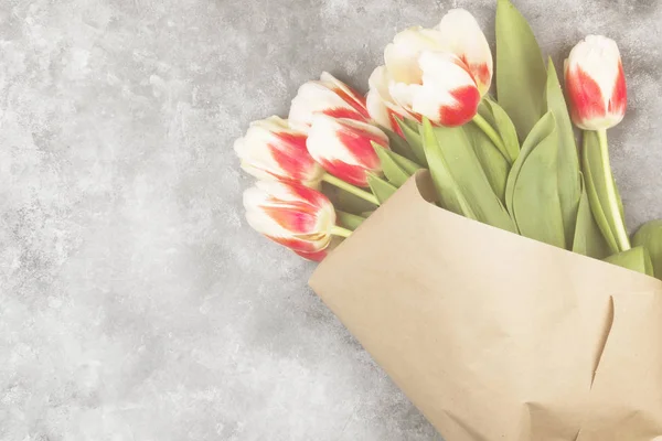 Bouquet of red-white tulips in kraft paper on a light background. Top view, copy space. Toning.