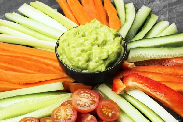 Guacamole de sauce traditionnelle latino-américaine dans un bol et divers légumes (carottes, tomates, concombres, céleri) sur fond sombre . — Photo