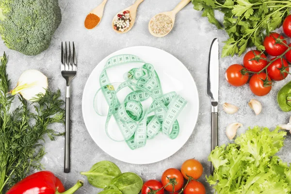 Concepto de comida dietética. Placa blanca y cinta métrica. Varias verduras y especias (brócoli, pimienta, tomates cherry, ajo, lechuga, perejil, hinojo) sobre un fondo claro — Foto de Stock